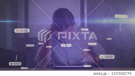 Leaning adult male wearing gray shirt studying tablet at office desk, with notification icons 133508774