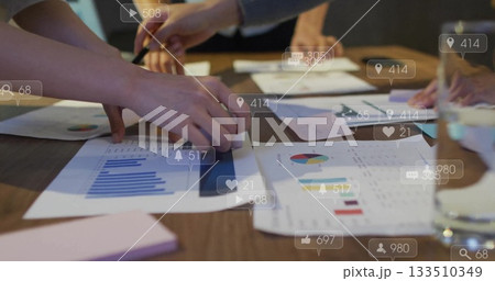 Examining professionals in suits pointing at printed graphs on meeting table with pen, sticky pad 133510349