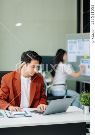 Confident Asian man with a smile standing holding notepad and tablet at office. Confident Asian man with a smile standing holding notepad and tablet at office. 133511053