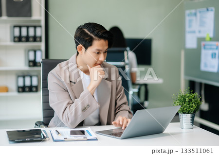 Confident Asian man with a smile standing holding notepad and tablet at office. Confident Asian man with a smile standing holding notepad and tablet at office. 133511061