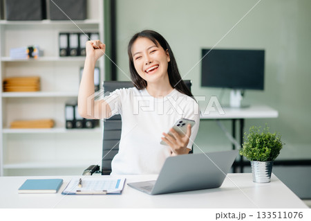 Confident Asian woman with a smile standing holding notepad and tablet at office. Confident Asian woman with a smile standing holding notepad and tablet at office. 133511076