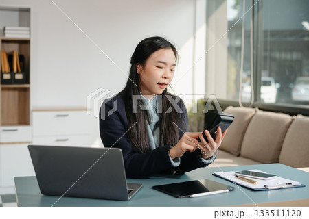 Asian businesswoman working with working notepad, tablet and laptop documents talking on the smartphone, tablet and laptop video call tax, report, accounting 133511120