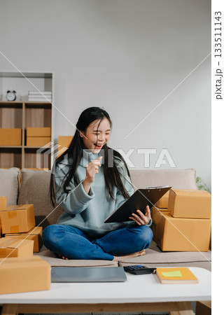 woman using smartphone or tablet taking receive and checking online purchase shopping order to preparing pack product box. woman using smartphone or tablet taking receive and checking online purchase shopping order to preparing pack product box. 133511143