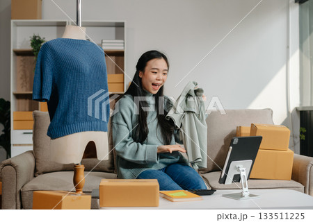 Asian lady blogger showing clothes in front of the camera to recording vlog video live streaming at her shop. Online Shopping Cart notion. 133511225