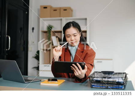 Asian businesswoman working with working notepad, tablet and laptop documents talking on the smartphone, tablet and laptop video call tax, report, accounting Asian businesswoman working with working notepad, tablet and laptop documents talking on the smartphone, tablet and laptop video call tax, report, accounting 133511335