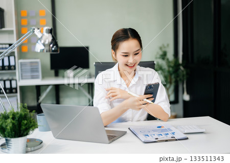 Asian woman with a smile standing holding notepad and tablet at the office. Asian woman with a smile standing holding notepad and tablet at the office. 133511343