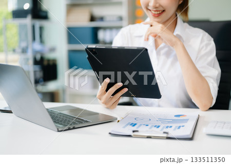Asian woman with a smile standing holding notepad and tablet at the office. Asian woman with a smile standing holding notepad and tablet at the office. 133511350