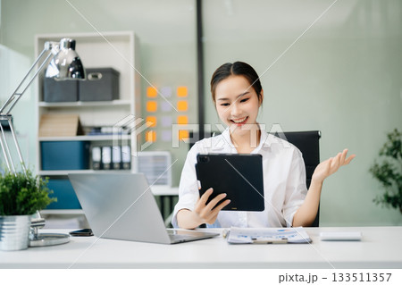Asian businesswoman working with working notepad, tablet and laptop documents talking on the smartphone, tablet and laptop video call tax 133511357