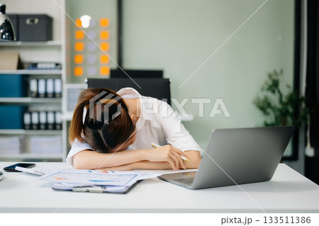 Overworked young Asian businesswoman office worker suffering from neck pain after had a long day at her office desk. 133511386