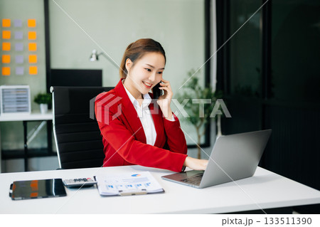 Asian businesswoman working with working notepad, tablet and laptop documents talking on the smartphone, tablet and laptop video call tax 133511390
