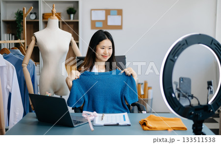 Asian lady blogger showing clothes in front of the camera to recording vlog video live streaming at her shop. 133511538