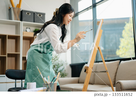 Asian Female painter do artwork in art workshop, painting supplies, oil pastels, two canvas easel, creative space 133511652