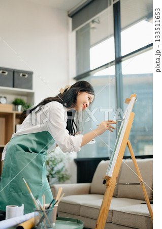 Asian Female painter do artwork in art workshop, painting supplies, oil pastels, two canvas easel, creative space 133511653