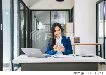 Young Asian businesswoman working with working notepad, tablet and laptop documents talking on the smartphone, tablet and laptop video call 133511741