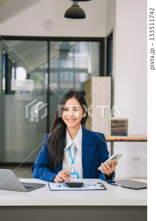 Young Asian businesswoman working with working notepad, tablet and laptop documents talking on the smartphone, tablet and laptop video call 133511742