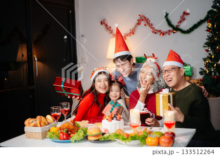 Joyful Asian family gathered for a Christmas feast, exchanging gifts, and celebrating the holiday season with love Joyful Asian family gathered for a Christmas feast, exchanging gifts, and celebrating the holiday season with love 133512264