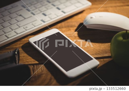 Smartphone is sitting on wood desk in flat design, with keyboard and mouse, flashlight, green apple Smartphone is sitting on wood desk in flat design, with keyboard and mouse, flashlight, green apple 133512660