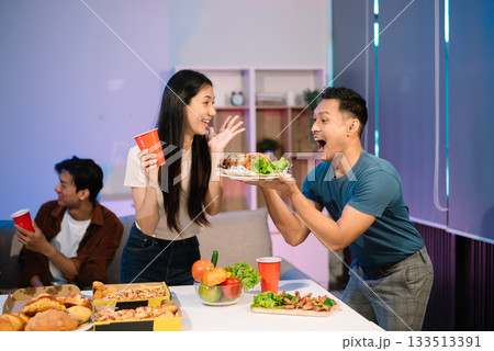 Young Asian Friends Celebrating with Laughter and Food at a Modern Evening Party 133513391