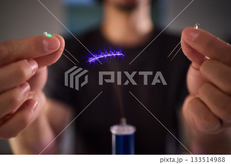 Hands manipulating metal spheres generate vibrant electrical plasma display, Laboratory scene showcasing coil discharging luminous sparks with scientific precision 133514988