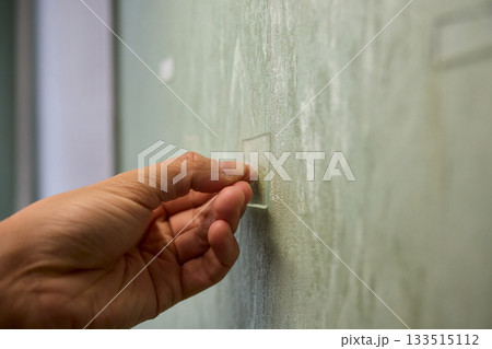 Closeup of textured plaster wall prep, Gently detaching thin tape from wall surface, Homeowner carefully removing adhesive strip to ready wall for repainting process Closeup of textured plaster wall prep, Gently detaching thin tape from wall surface, Homeowner carefully removing adhesive strip to ready wall for repainting process 133515112