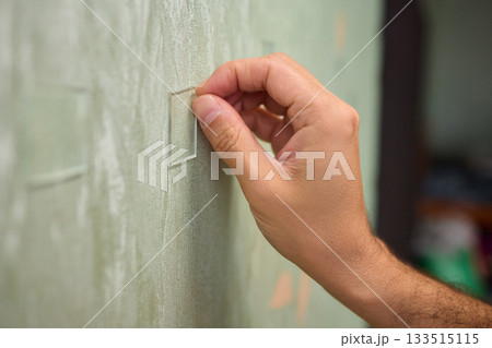 Closeup of textured plaster wall prep, Gently detaching thin tape from wall surface, Homeowner carefully removing adhesive strip to ready wall for repainting process Closeup of textured plaster wall prep, Gently detaching thin tape from wall surface, Homeowner carefully removing adhesive strip to ready wall for repainting process 133515115