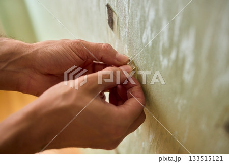 Closeup of textured plaster wall prep, Gently detaching thin tape from wall surface, Homeowner carefully removing adhesive strip to ready wall for repainting process 133515121