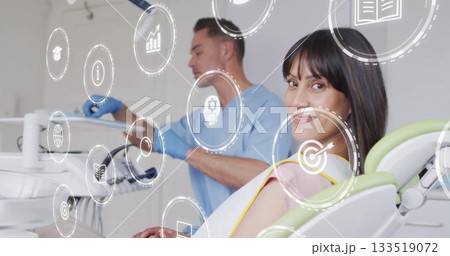 Smiling female patient reclining on chair in clinic room, with tray and digital icons, copy space 133519072