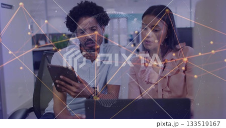 Two professionals viewing tablet and pointing at laptop in modern office, network map Two professionals viewing tablet and pointing at laptop in modern office, network map 133519167