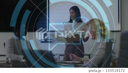 Presenting woman in blouse and skirt discussing report at conference table, with folder and screen 133519172