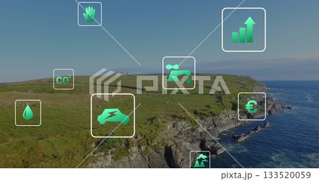 Displaying grassy coastal cliff overlooking deep blue sea, with floating green sustainability icons 133520059
