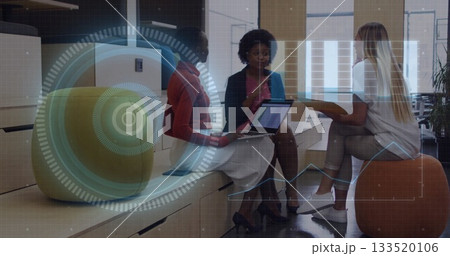 Women in business attire discussing holographic projections in office lounge, sitting on stool Women in business attire discussing holographic projections in office lounge, sitting on stool 133520106