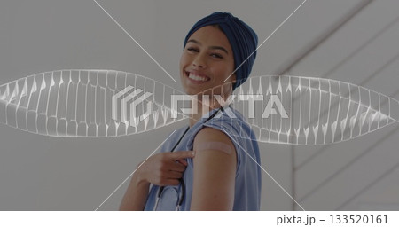 Smiling medical worker in scrubs and turban pointing to vaccine bandage at clinic hall, stethoscope 133520161