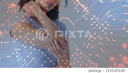 Standing woman wearing blue shirt holding right elbow inside room, with digital circuit overlay Standing woman wearing blue shirt holding right elbow inside room, with digital circuit overlay 133520189