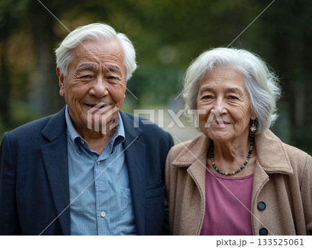 Portrait of a happy senior couple with white hair, smiling warmly at the camera outdoors in a park setting with blurred green background and natural light 133525061