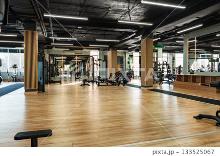 Modern gym interior with wooden flooring and various workout equipment in use Modern gym interior with wooden flooring and various workout equipment in use 133525067
