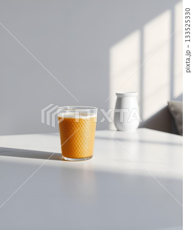 A refreshing glass of orange juice stands on a white table, illuminated by sunlight. 133525330