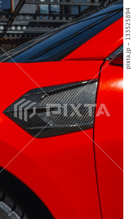 Close-up view of sleek red car showcasing unique carbon fiber details during daylight Close-up view of sleek red car showcasing unique carbon fiber details during daylight 133525894