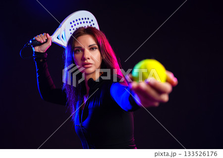 Athletic woman preparing to hit a ball with a paddle in dramatic lighting setting 133526176