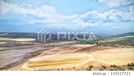 Arid farmland is being illustrated in flat vector style, showing plowed fields, dirt tracks, hills Arid farmland is being illustrated in flat vector style, showing plowed fields, dirt tracks, hills 133527721