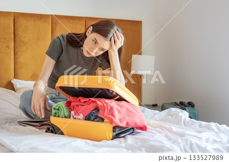 Woman feeling frustrated struggling packing clothes into luggage Woman feeling frustrated struggling packing clothes into luggage 133527989
