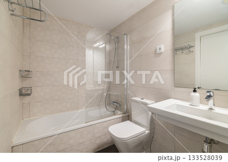 Modern bathroom with a shower and bathtub. White tiles cover the walls. A sink with a mirror is visible. Clean and minimalistic design. 133528039