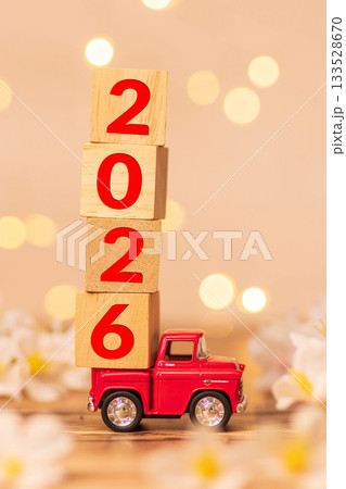red truck toy carrying wooden cube with number 2026 in the back of the pickup for start of beginning new year 2026 with blur white flower field and defocus sparkling bokeh light at background 133528670