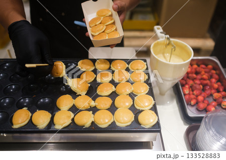 Baker prepares mini pancakes with strawberries in a lively kitchen Baker prepares mini pancakes with strawberries in a lively kitchen 133528883