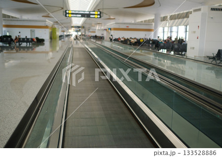 Busy airport terminal features moving walkway and seating area with passengers waiting for their flights Busy airport terminal features moving walkway and seating area with passengers waiting for their flights 133528886