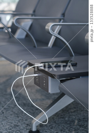 Charging station at an airport seating area with a smartphone plugged into an outlet during busy travel hours 133528888
