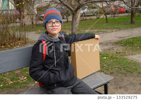 teenager sits on a grey bench with a box looking straight ahead teenager sits on a grey bench with a box looking straight ahead 133529275