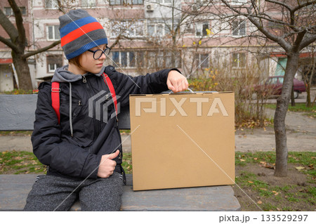 teenager sits on a bench holding a box by the handle looks to the side teenager sits on a bench holding a box by the handle looks to the side 133529297