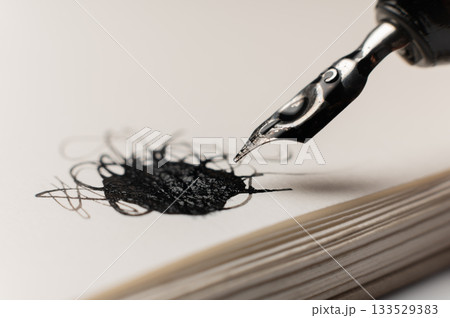 black pen next to a white notebook. An office desk with a notebook and fountain pen. A stylish modern pen and ink blot on a white background black pen next to a white notebook. An office desk with a notebook and fountain pen. A stylish modern pen and ink blot on a white background 133529383