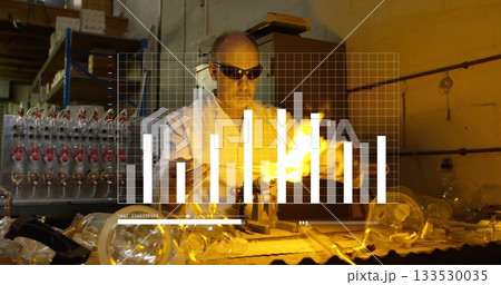 Goggled glassblower working at workbench shaping glass tubing by torch flame, digital chart overlay 133530035