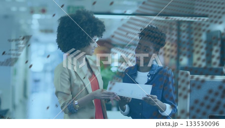 Two women in blazer and plaid shirt reviewing printed document in open office, red dot partition 133530096